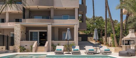 Un edificio moderno de varios pisos con piscina, mobiliario exterior y palmeras.