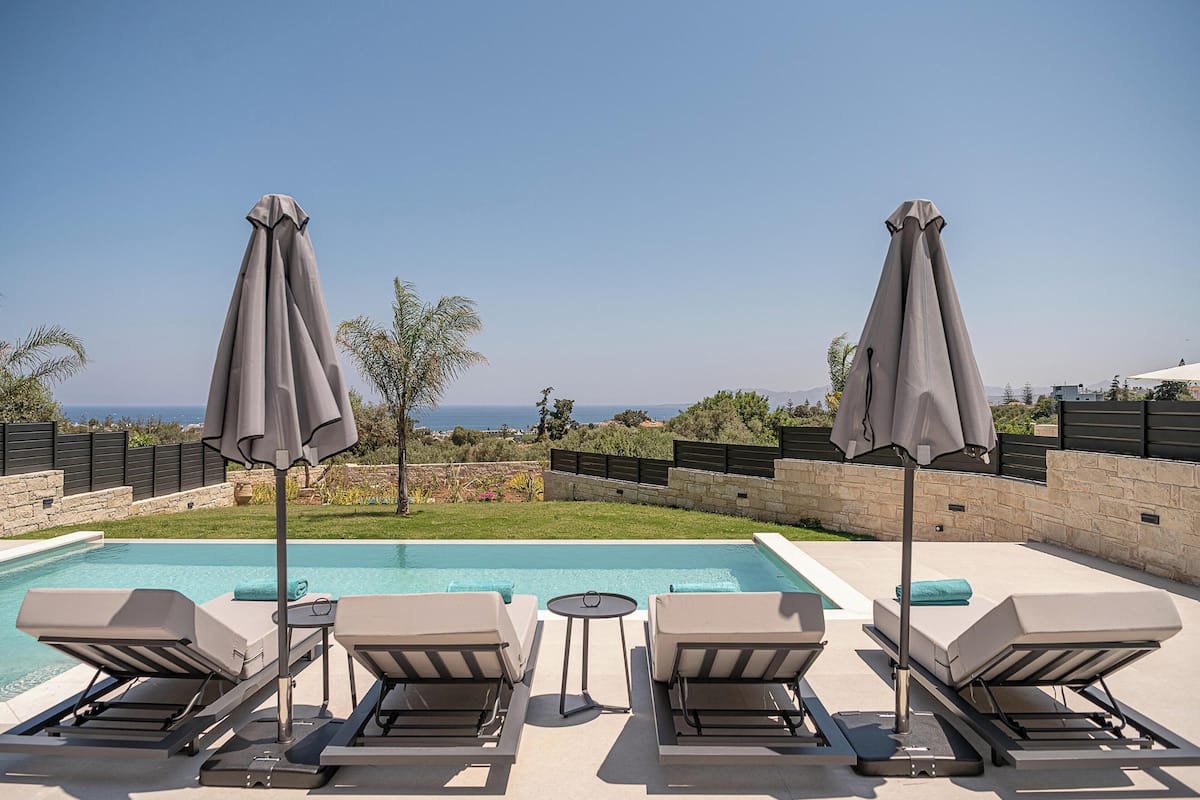 A poolside area with lounge chairs and umbrellas, a small table, and a view of the sea.