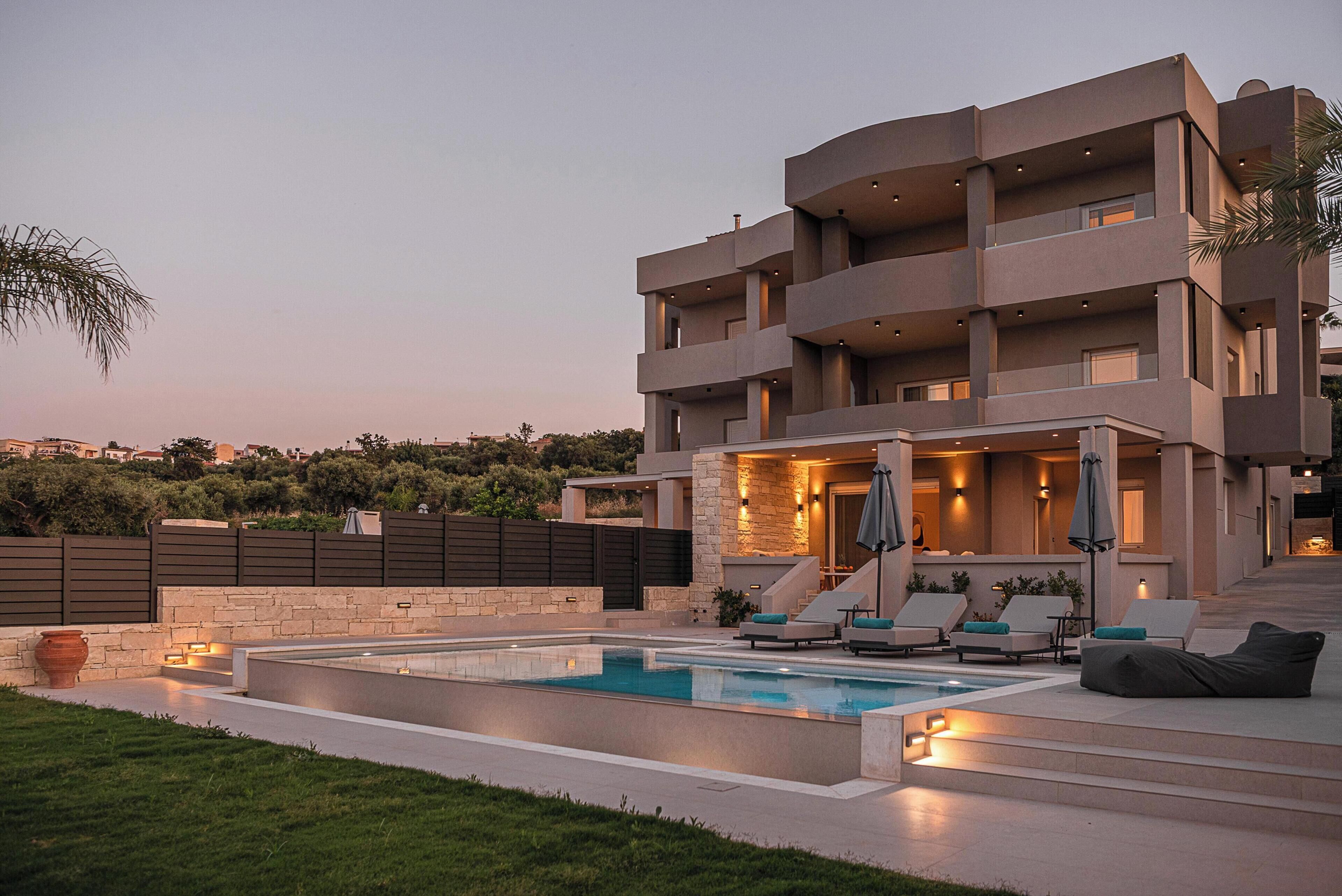 A modern multi-story building with a swimming pool, outdoor seating, and a stone wall.