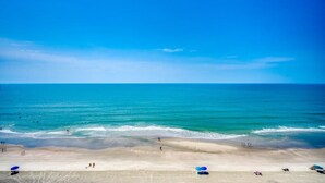 A beach with clear blue water, sandy shore, and umbrellas. - Oceanfront Modern Home w Lazy River and Pools (North Myrtle Beach)
