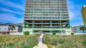 A multi-story hotel with a central courtyard, balconies, and a sandy pathway leading to the entrance. - Oceanfront Modern Home w Lazy River and Pools (North Myrtle Beach)