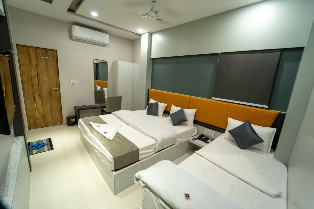 A hotel room with two beds, a wooden door, an air conditioning unit, a mirror, and a bedside table.