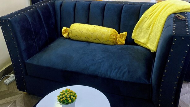 Um sofá azul escuro com detalhes amarelos e uma mesa branca com uma pequena planta.