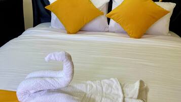Una cama bien hecha con ropa blanca, dos almohadas amarillas y una toalla blanca con forma de cisne sobre un edredón naranja.