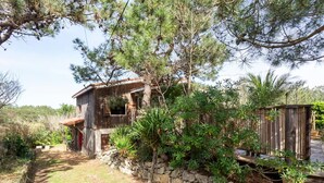 Ein rustikales Holzhaus mit einer Steinwand, umgeben von dichtem Grün und Bäumen.