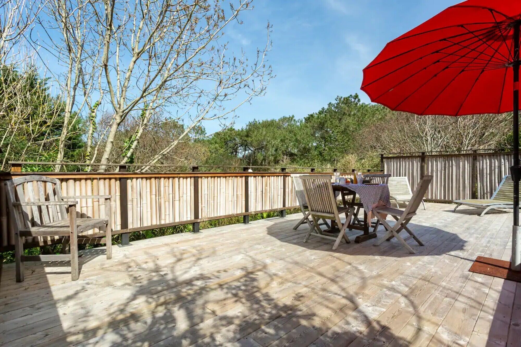Una terraza de madera con una mesa, sillas, un paraguas rojo y una valla de madera.