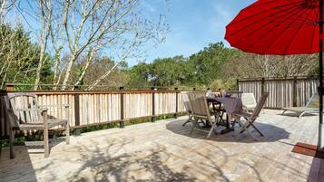 Una terraza de madera con una mesa, sillas, un paraguas rojo y una valla de madera.