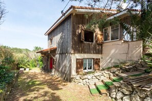 A rustic two-story house with a stone foundation, wooden siding, and a red door.