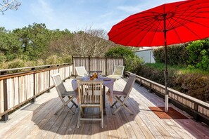 Une terrasse en bois avec une table et des chaises, un parasol rouge et une clôture en bois.