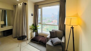 A modern hotel room with a large window, a sofa, a standing lamp, and a small table with a plant.