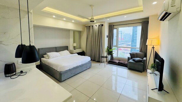 A modern hotel room with a large bed, a desk, a chair, a TV, and a view of the city.