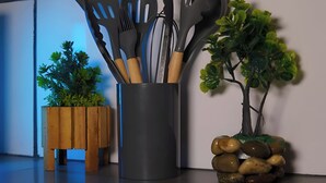 A kitchen counter with a utensil holder containing various kitchen tools, a small wooden planter with a plant, and a decorative rock arrangement.