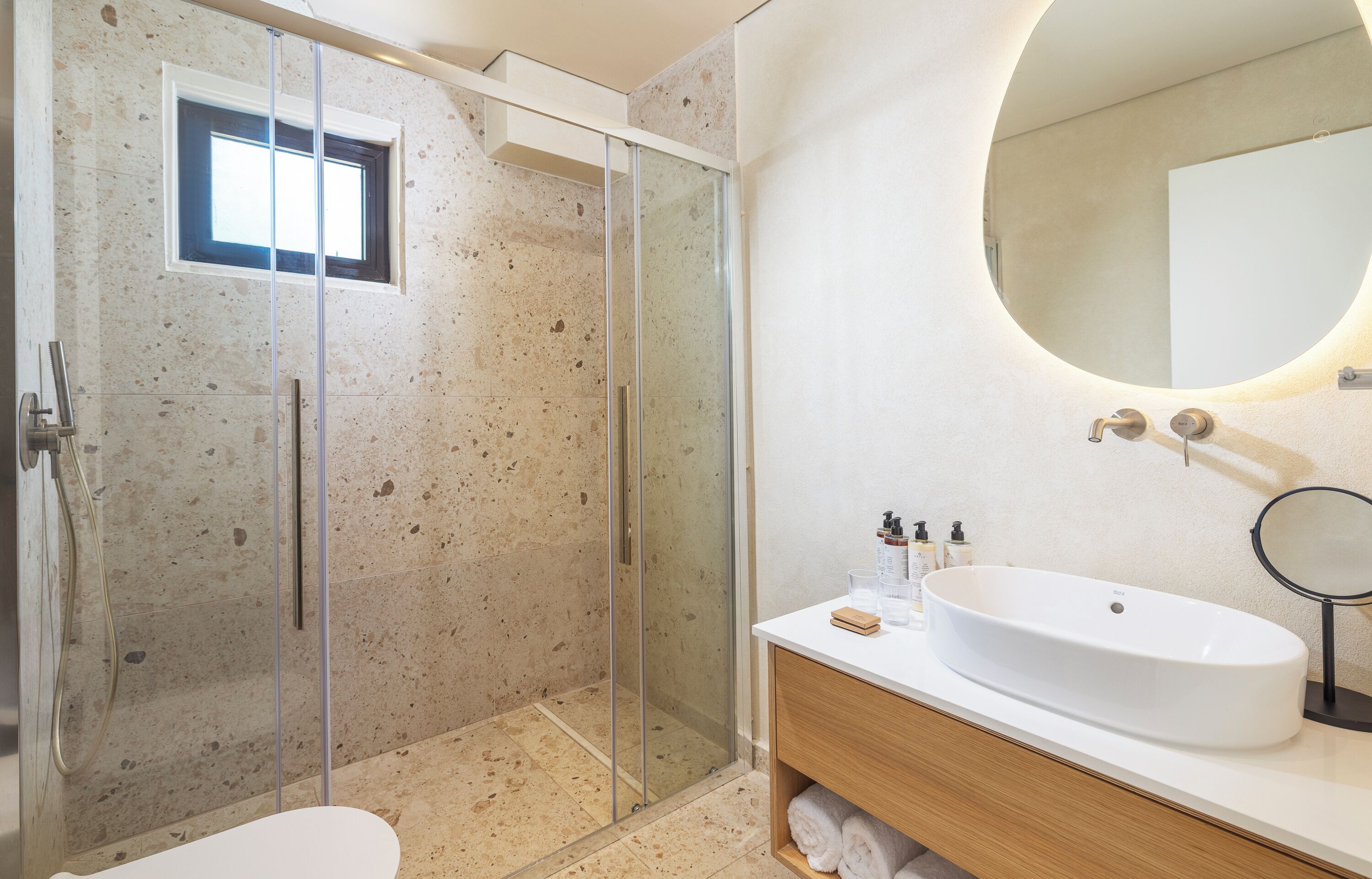 Een moderne badkamer met een glazen douchecabine, een ronde spiegel en een witte wastafel.