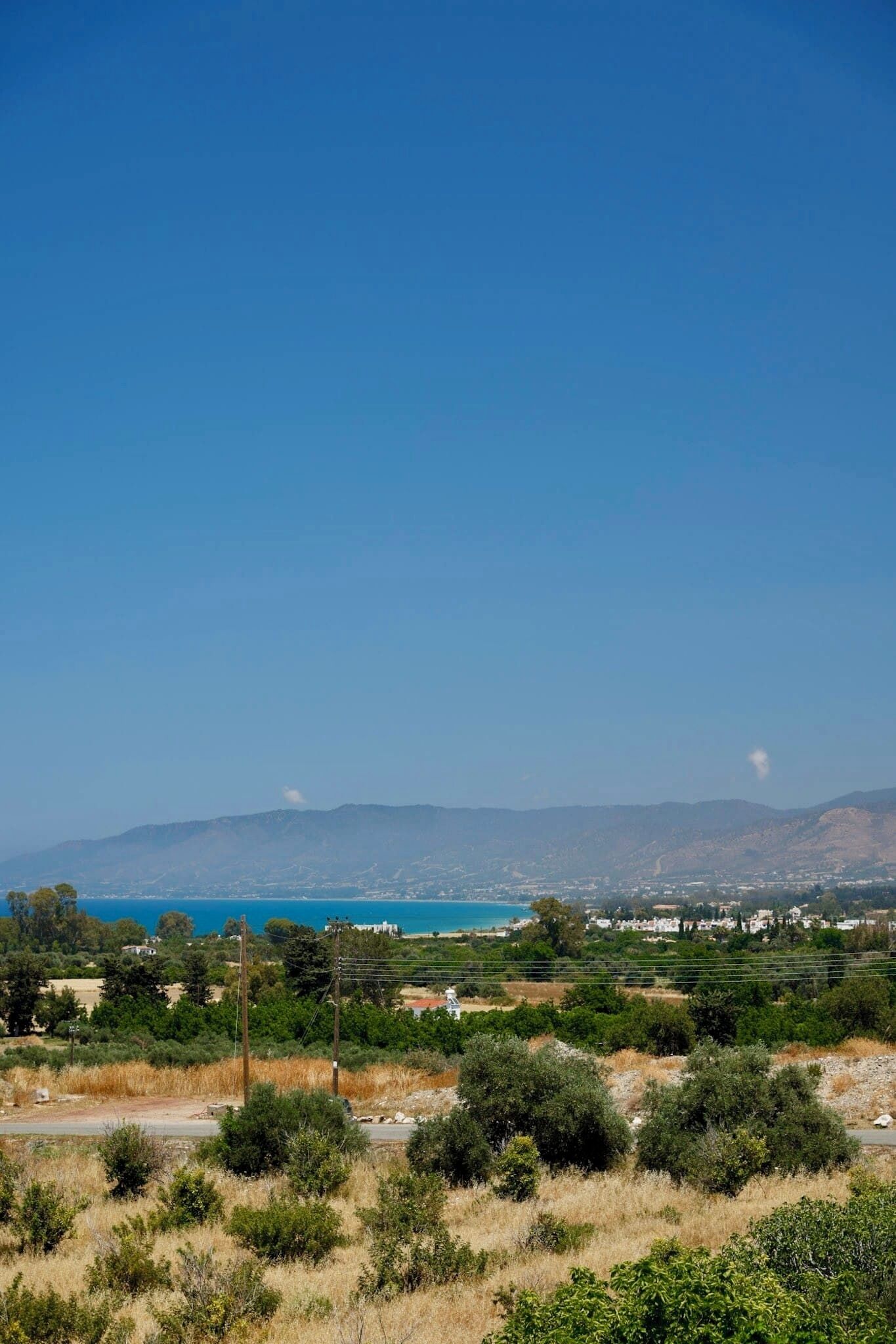 A coastal landscape with a clear sky, distant mountains, and a view of the sea.