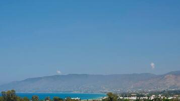 A coastal landscape with a clear sky, distant mountains, and a view of the sea.