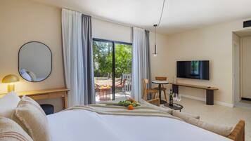 Habitación de hotel con cama, escritorio, silla, televisión y balcón con vistas a árboles.
