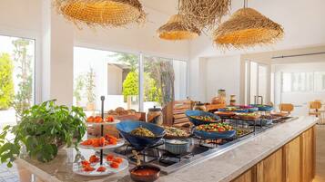 A buffet setup with various dishes, a large plant, and wicker ceiling lights.