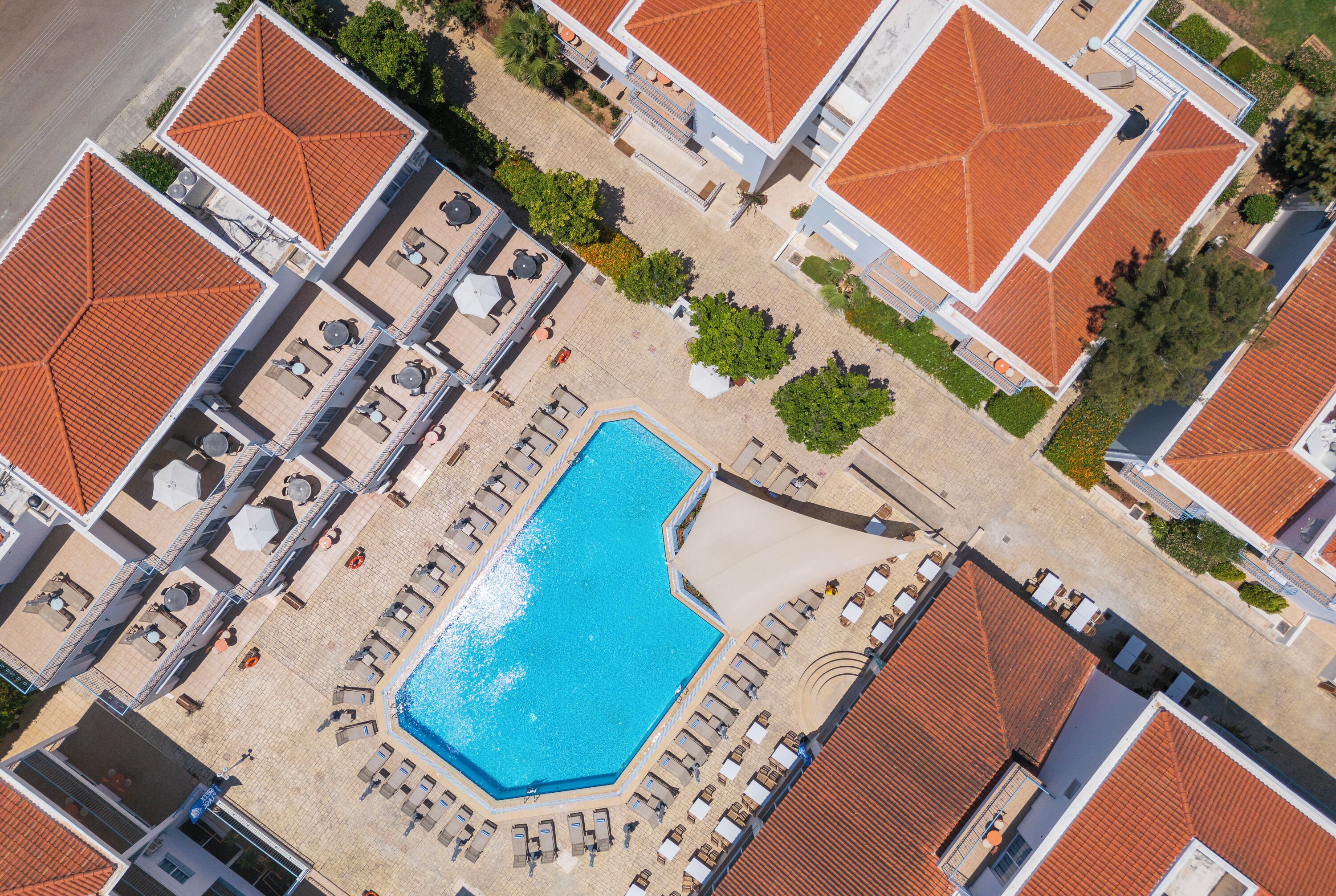 An aerial view of a hotel with a swimming pool, multiple rooms with red-tiled roofs, and outdoor seating areas.
