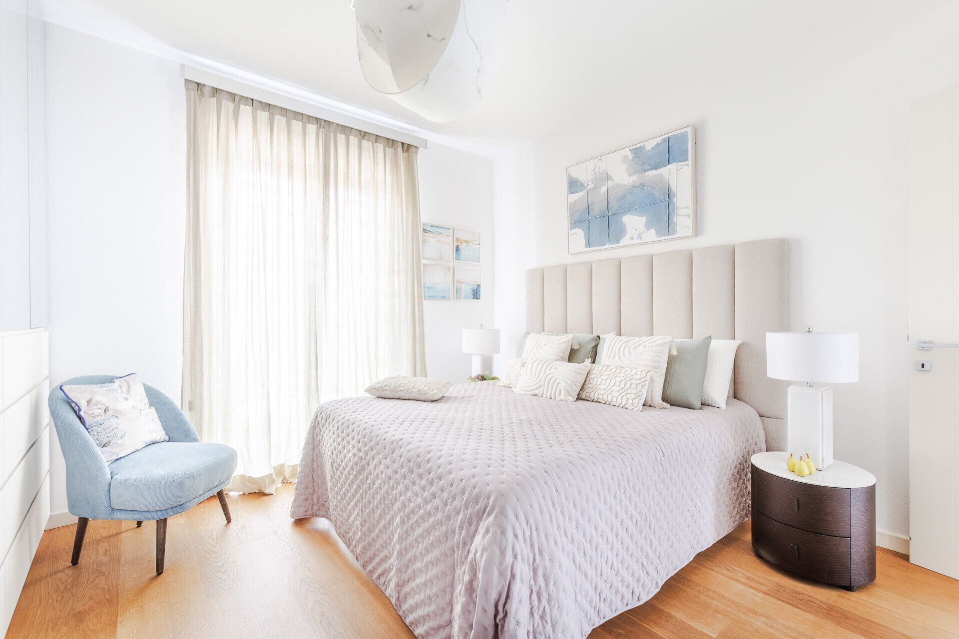 A bedroom with a large bed, a chair, a bedside table, and a painting on the wall.