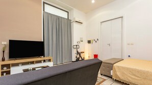 A modern room with a flat-screen TV, a sofa, a bed, a desk with a computer, and a window with curtains. - Apartment 'Giulia's Home - Borgo' with Private Terrace, Wi-Fi and Air Conditioning (Catania)