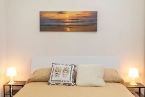 Une chambre à coucher comprenant un lit, deux lampes de chevet, une table de chevet, un tableau accroché au mur et deux oreillers.