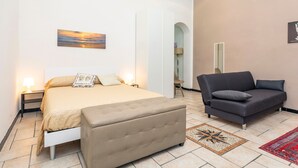 A bedroom with a bed, a sofa, a nightstand, a lamp, and a painting on the wall. - Apartment 'Giulia's Home - Borgo' with Private Terrace, Wi-Fi and Air Conditioning (Catania)