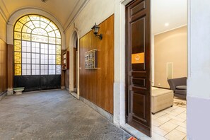 Un couloir avec une porte en bois, une porte en verre ornée d’un motif géométrique et un sol carrelé.