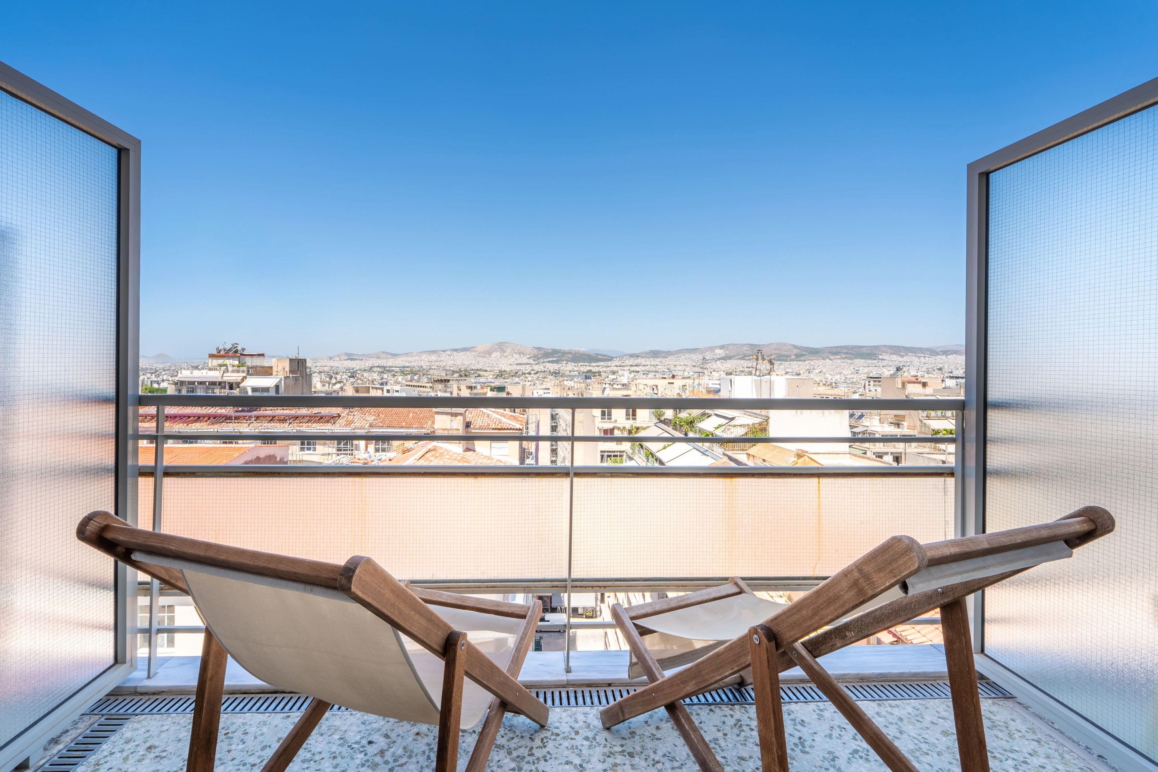 Un balcon offrant une vue sur le paysage urbain, avec une chaise en bois et une rambarde en métal.