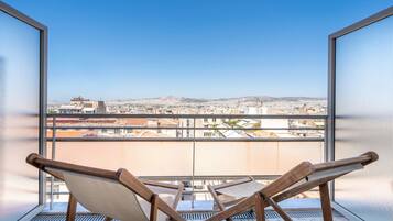 A balcony with a view of a cityscape, featuring a wooden chair and a metal railing.