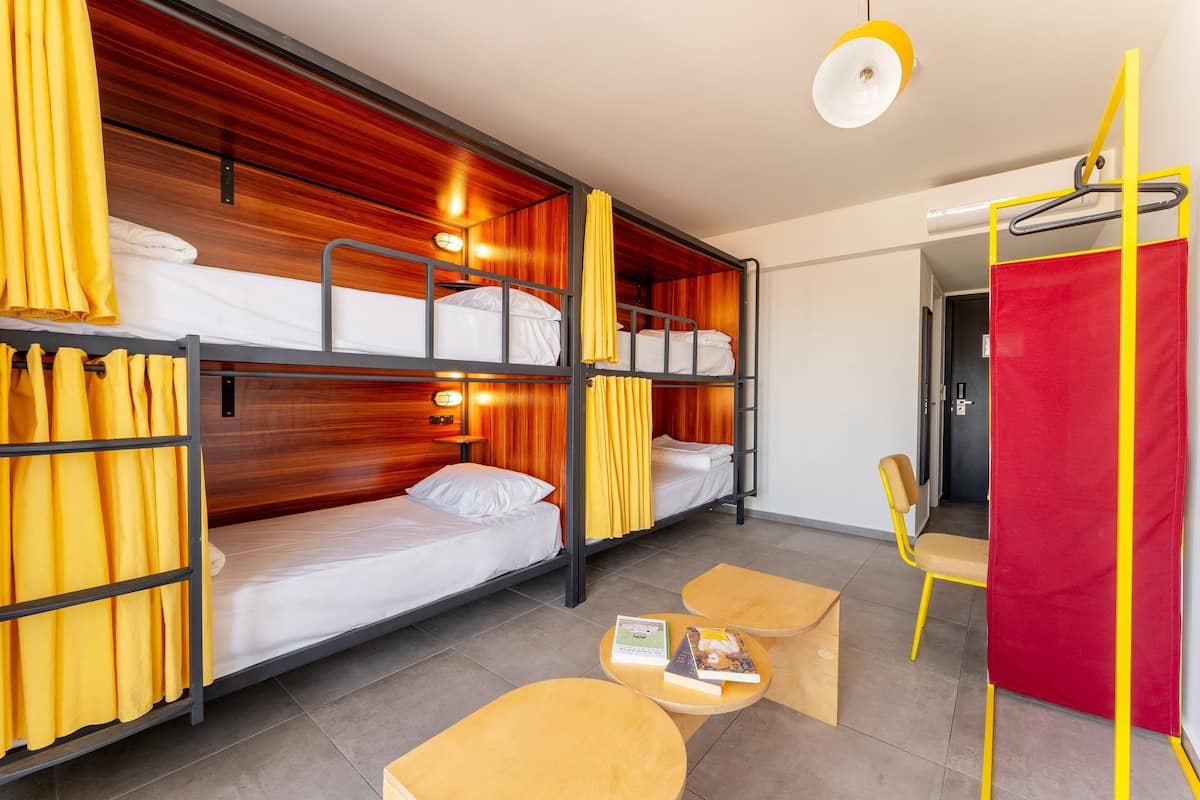Une chambre de dortoir avec des lits superposés, un paravent rouge, une chaise et une table avec des livres.