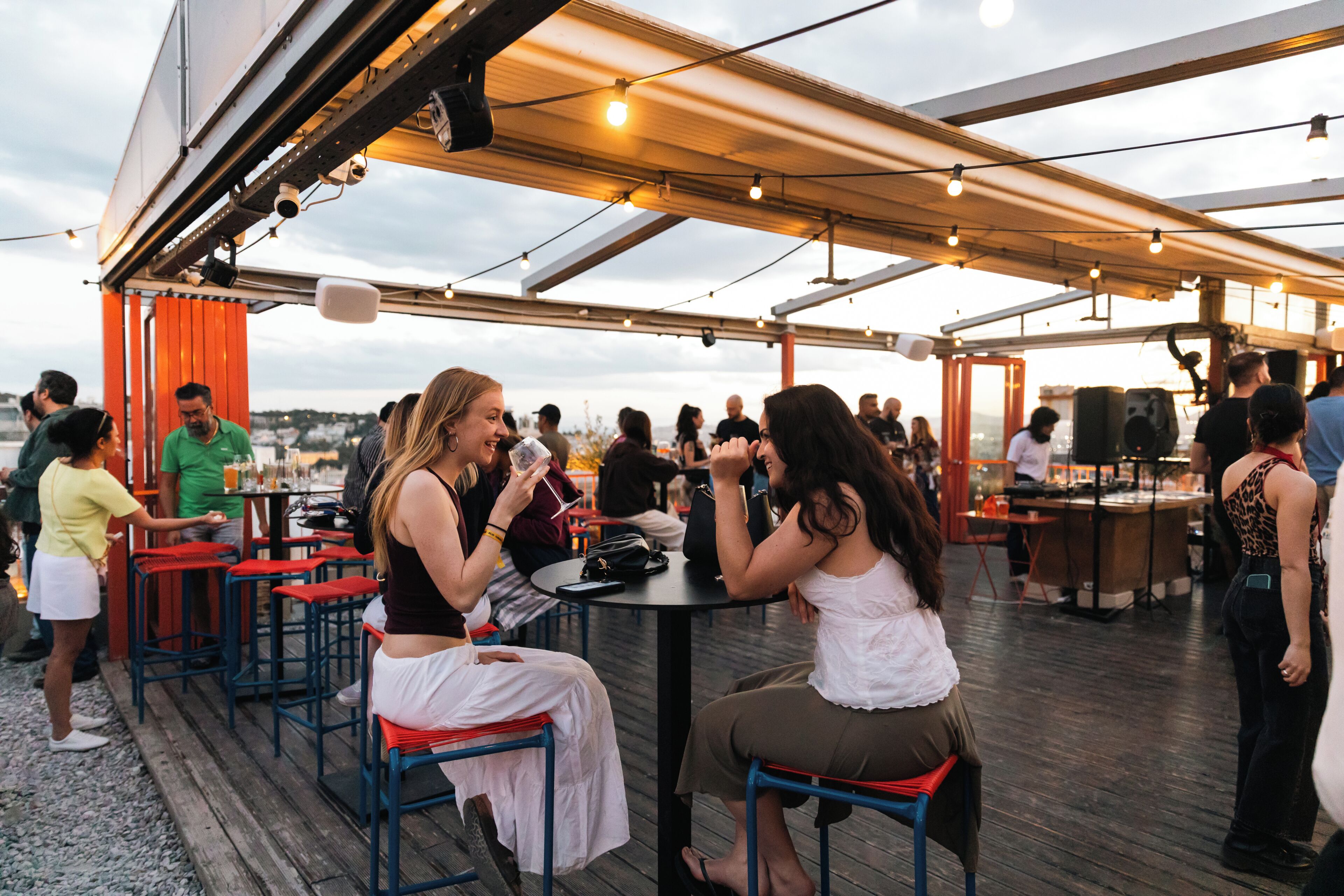 An outdoor dining area with tables and chairs, a covered section, and a view of the cityscape.