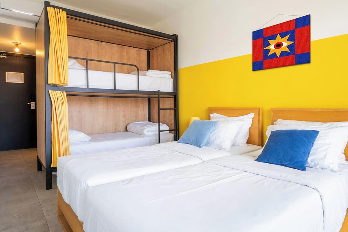 Une chambre d’hôtel avec deux lits simples et un lit superposé, le tout dans une pièce aux murs jaunes.