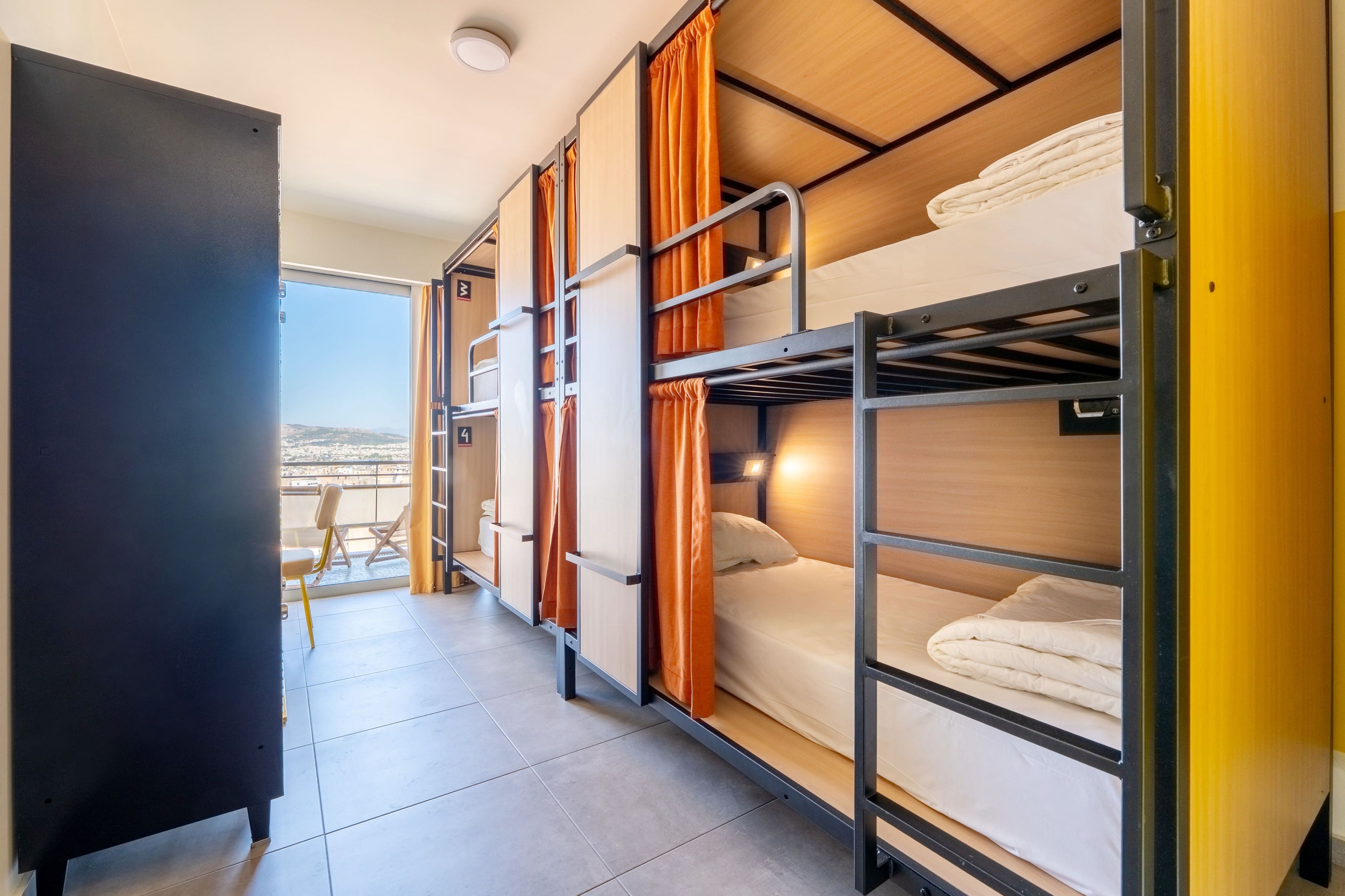 A dormitory room with bunk beds, a desk, and a window with a view.