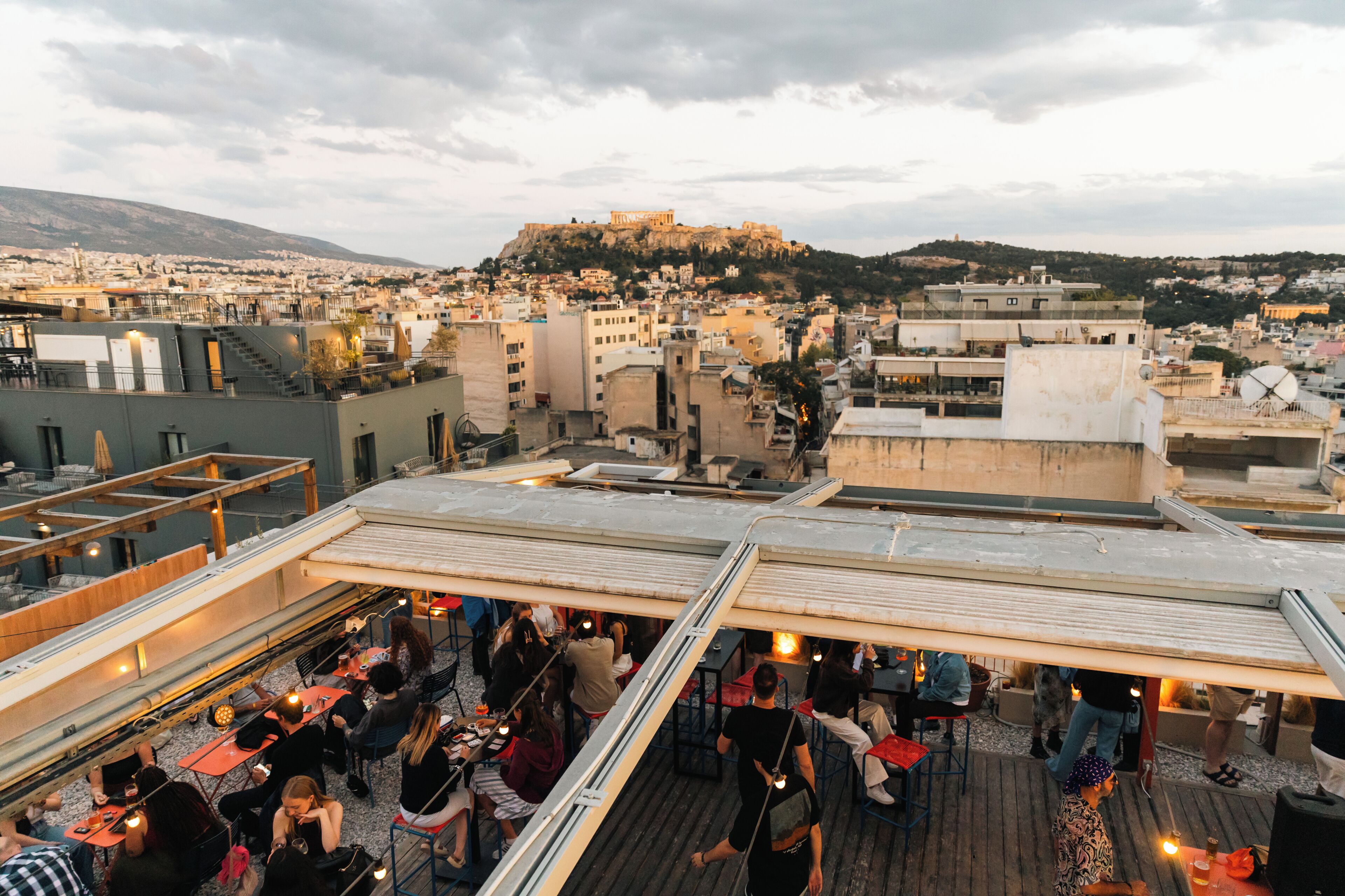 A rooftop bar with outdoor seating, overlooking a cityscape and a hill with ruins.