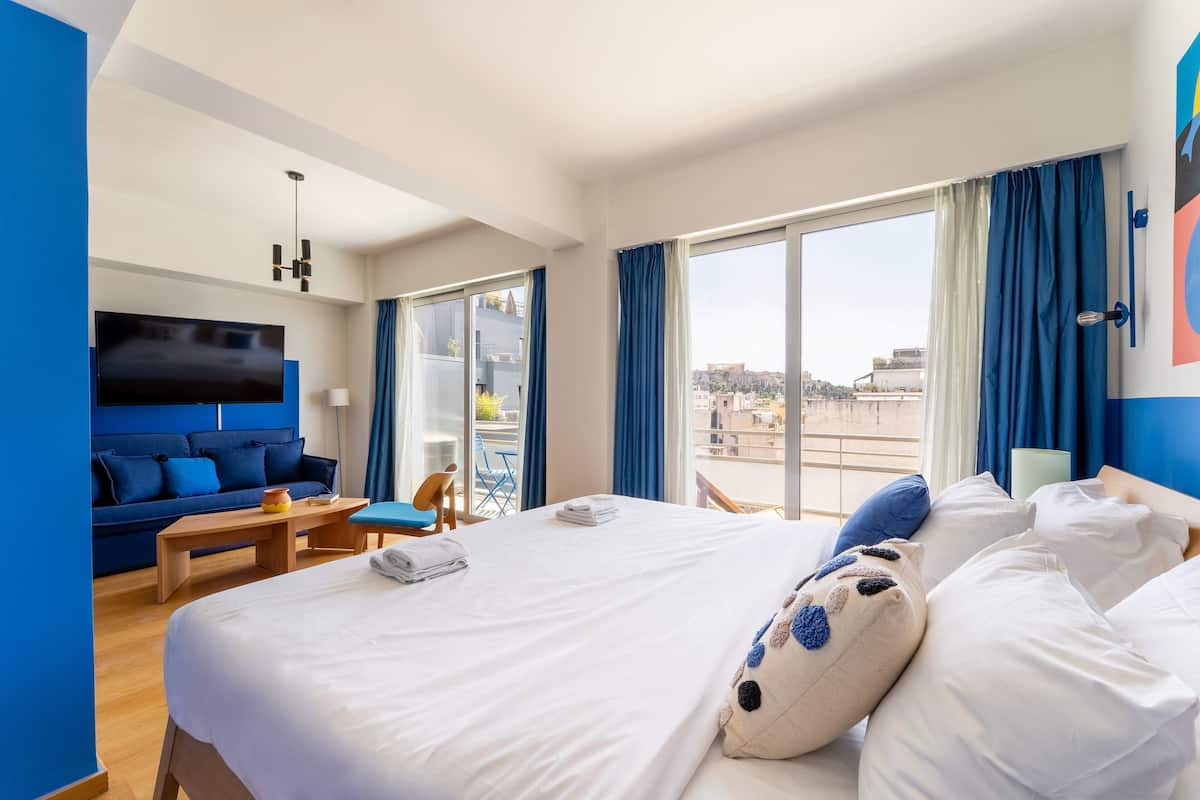 Une chambre d’hôtel avec un grand lit, un canapé, une télévision et un balcon agrémenté de rideaux bleus.