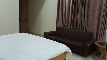 Un dormitorio con cama, sofá, una mesita y cortina.