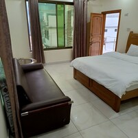 A hotel room with a bed, a sofa, a small table, and a window with curtains.