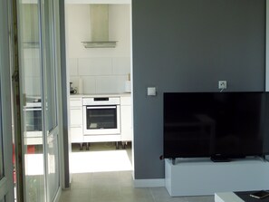 Una cocina moderna con armarios blancos, horno empotrado y televisor de pantalla plana montado sobre un soporte blanco.