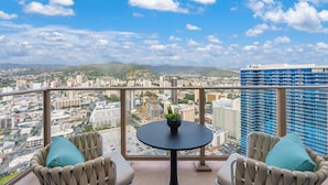 A balcony with a view of a cityscape, a small round table with a plant, and two chairs with cushions.