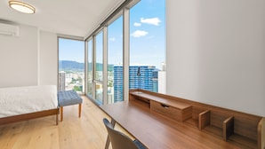 A modern bedroom with a large window, a wooden desk, and a bed.