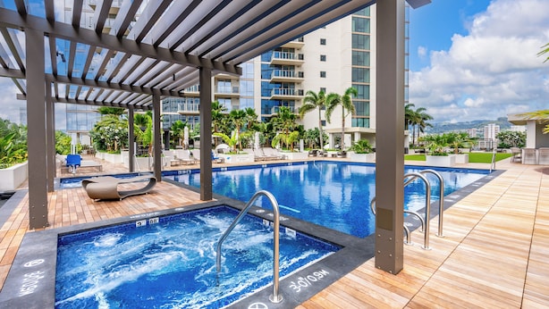 A rooftop pool area with a jacuzzi, lounge chairs, and a view of a modern building.