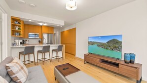 A modern living room with a sofa, a TV, and a kitchen area with wooden cabinets and a bar stool.