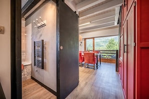 Een modern interieur met een houten vloer, een eethoek met rode stoelen en uitzicht op groen.