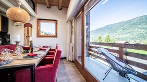A dining area with a wooden table, red chairs, and a view of a mountain landscape through large windows.