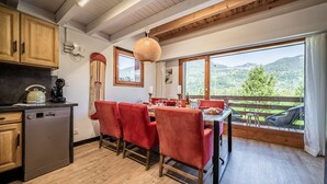 A dining area with a wooden table and red chairs, a kitchen with a dishwasher, and large windows with a mountain view.