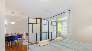 A modern hotel room with a bed, a desk with chairs, and a view of greenery outside. - LubuNest3 | Terrace with barbecue & private parking space (Ludwigsburg)