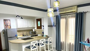 A compact kitchen with white cabinets, a built-in microwave, and a small island with bar stools. - Red Sea Breeze · Modern 1BR in Hadaba · Sharm El Sheikh (South Sinai Governorate)