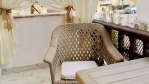 A balcony with a wicker chair and a wooden table, draped with sheer white curtains. - Red Sea Breeze · Modern 1BR in Hadaba · Sharm El Sheikh (South Sinai Governorate)