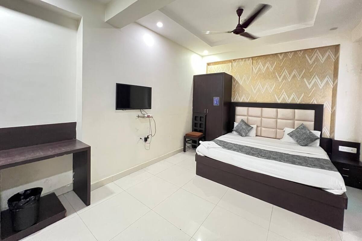Una habitación de hotel moderna con una cama grande, un televisor de pantalla plana en la pared, un ventilador de techo y un banco junto a la ventana.
