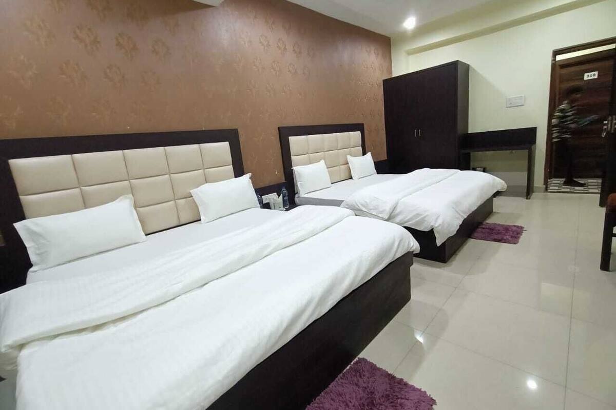 Habitación de hotel con tres camas, un armario y una pequeña mesa.